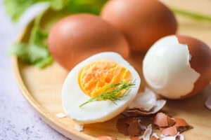 Perfect hard-boiled eggs sitting on a round wooden cutting board with one partially peeled and one egg interior exposed