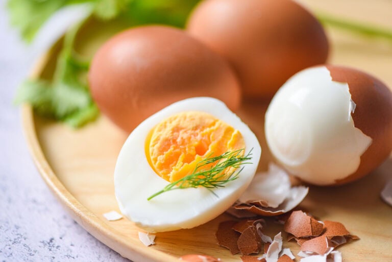 Perfect hard-boiled eggs sitting on a round wooden cutting board with one partially peeled and one egg interior exposed
